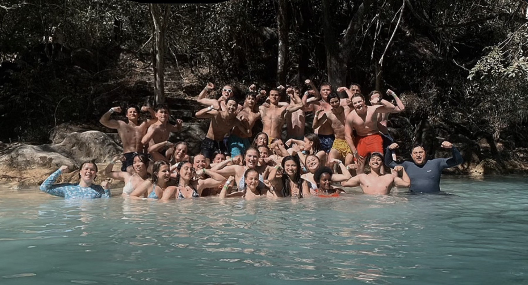 Grupo de viajeros celebrando dentro de una poza de aguas turquesa